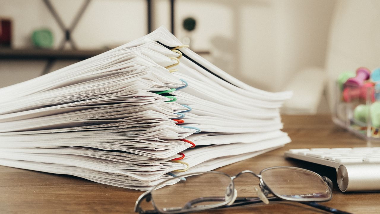 Accueil Close-up of a stack of office papers on a desk with glasses, emphasizing organization.